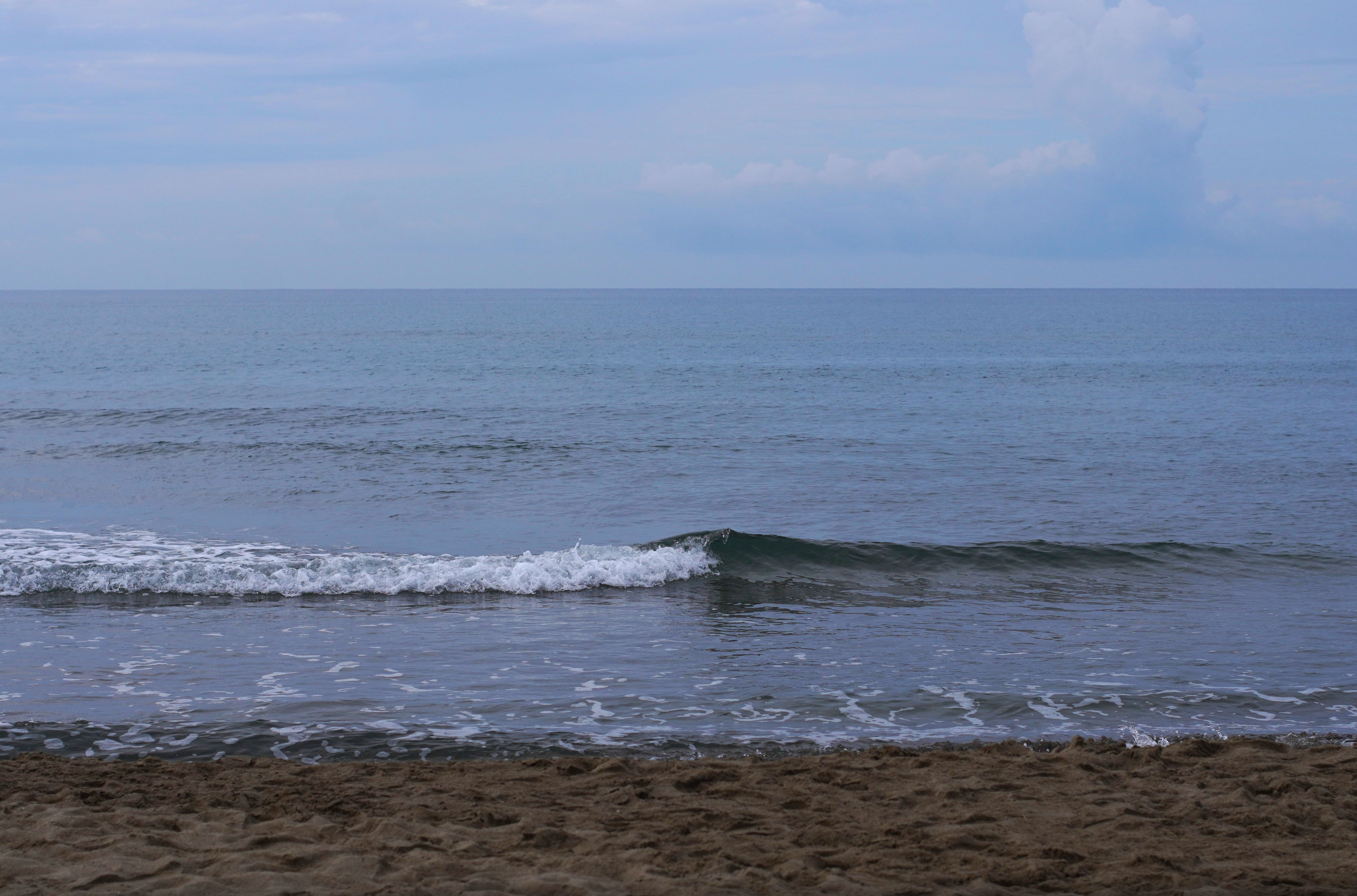 Sanfte Wellen am Sandstrand und ein weiter Blick über das Meer bis zum Horizont